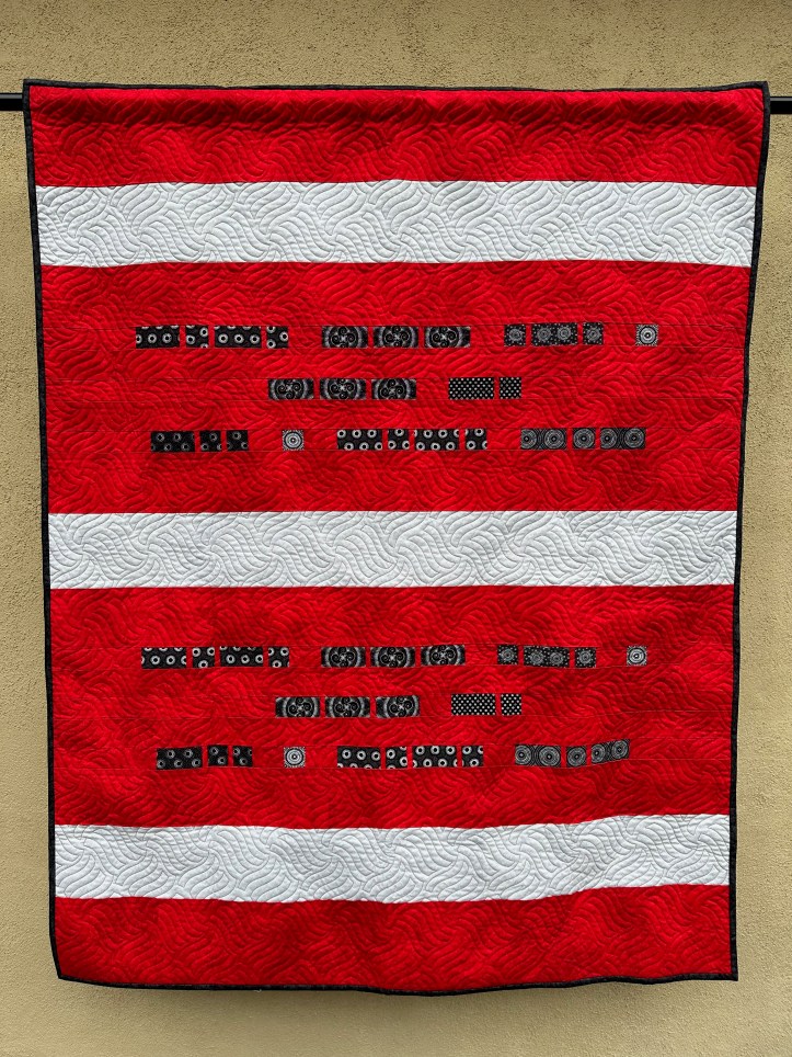 Hanging quilt with a Morse Code message in black on a red background