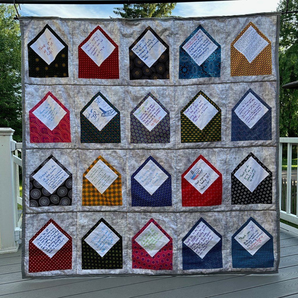 Hanging quilt, outdoors, that has 20 envelopes in rows and columns with thank-you notes in the envelopes
