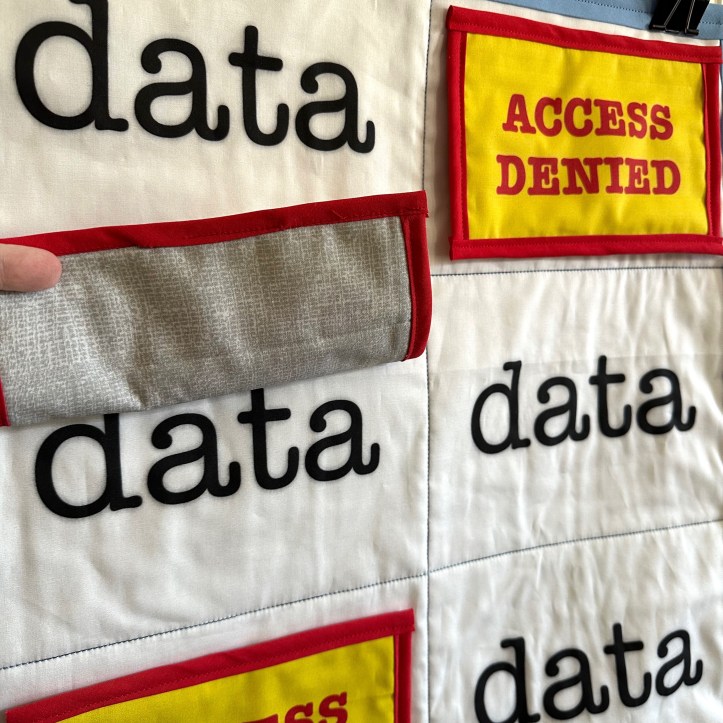 close-up of hanging quilt with the words data and yellow squares with red lettering stating access denied