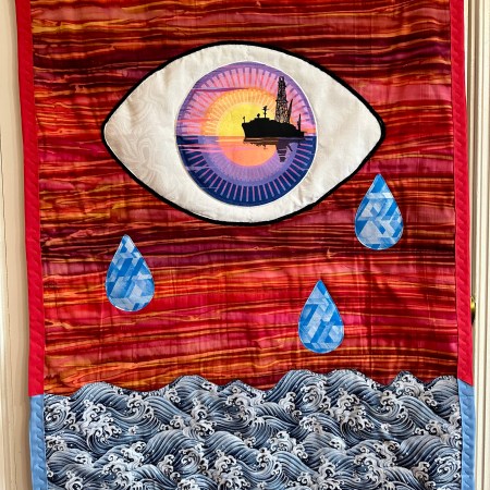 Hanging quilt with eye over a red sky and blue tears crying down into an ocean