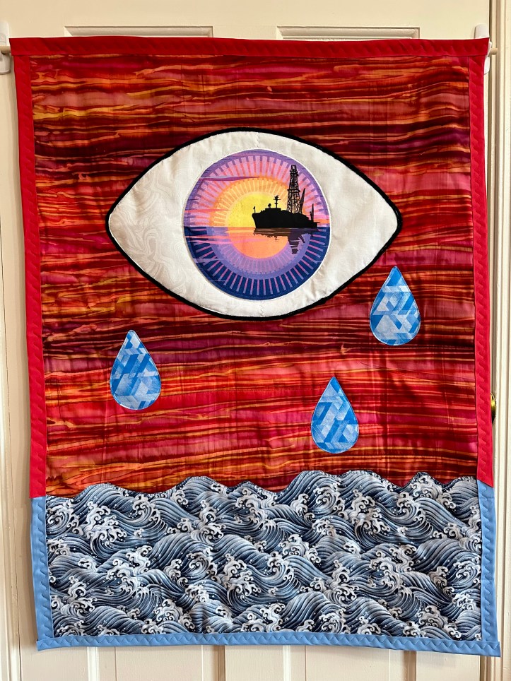Hanging quilt with eye over a red sky and blue tears crying down into an ocean