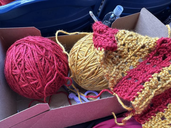 cardboard box with two balls of yarn (red and gold) and a crocheted piece in progress