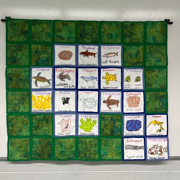 hanging quilt with green and white squares with images drawn on them